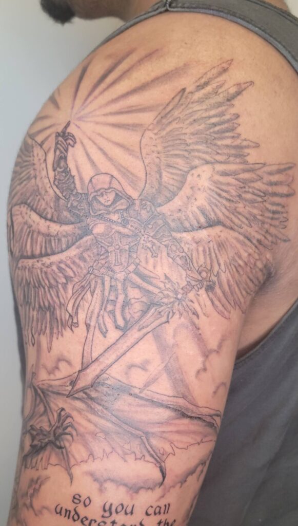 Angel warrior sleeve tattoo in black and grey with wings and sword, realistic religious tattoo on upper arm, fine line shading Calgary tattoo studio