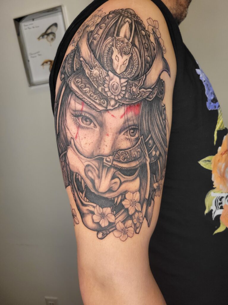Custom Japanese-inspired sleeve tattoo in Calgary featuring a samurai woman, Oni mask, dragon helmet, and cherry blossoms in black and grey realism by Angeloop Ink.